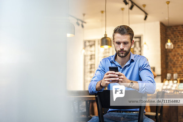 Junger Mann schaut auf Handy in einem Cafe