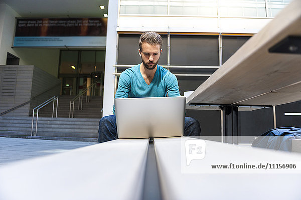 Junger Mann auf der Bank sitzend mit Laptop