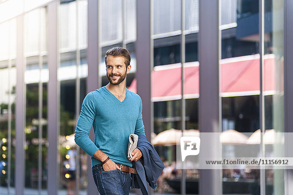 Lächelnder junger Mann  der eine Zeitung in der Stadt hält.