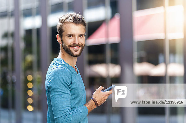 Lächelnder junger Mann mit Handy in der Stadt