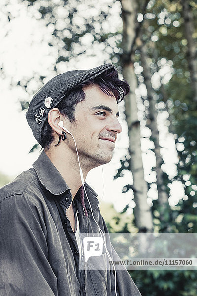 Lächelnder junger Mann mit Mütze  Musik hören mit Kopfhörern