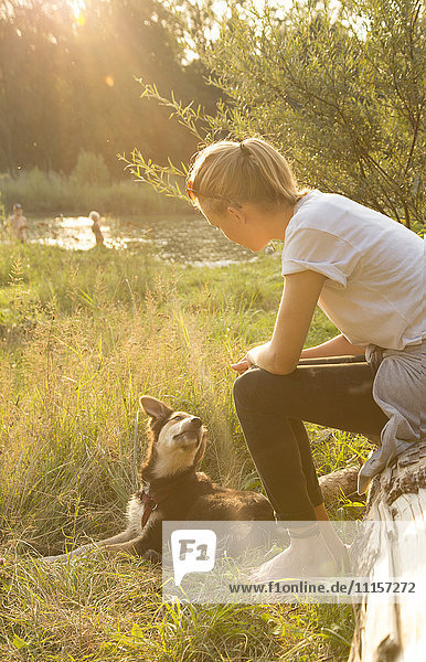 Junge Frau entspannt sich in der Abenddämmerung mit ihrem Hund in der Natur.
