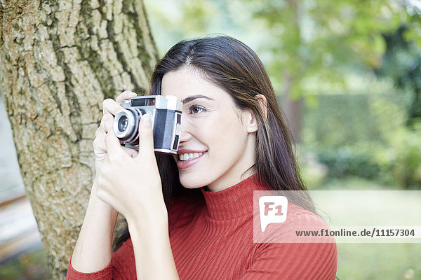 Lächelnde Frau beim Fotografieren mit Vintage-Kamera im Garten