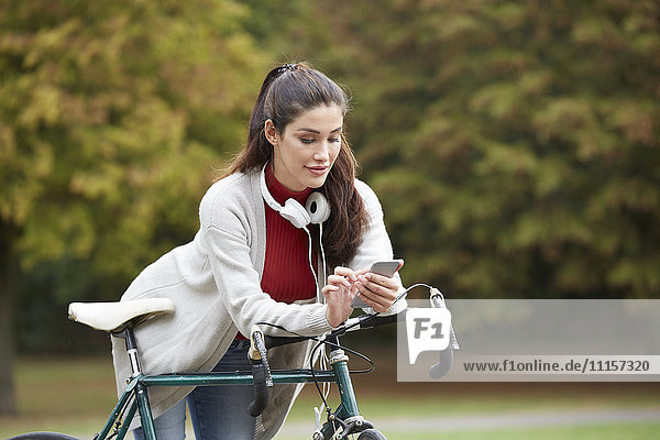 Woman with bicycle in an autumnal park text messaging