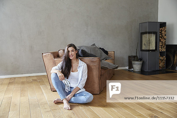 Lächelnde Frau auf dem Holzboden zu Hause sitzend