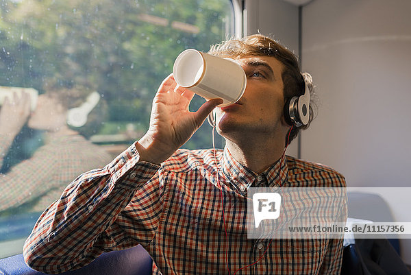 Junger Mann mit Kopfhörer  der Kaffee trinkt  um in einem Zug zu fahren.