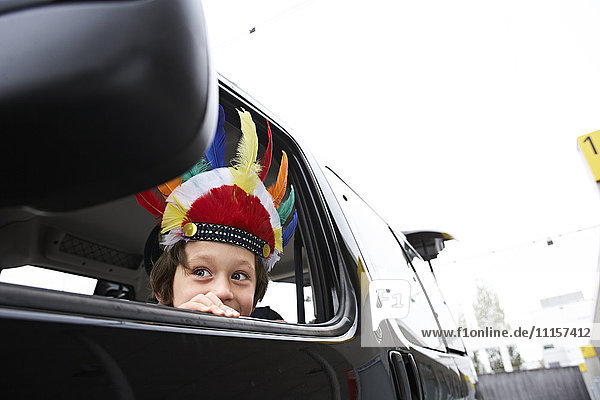 Boy with feather headdress looking out of car window