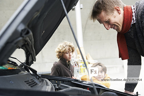 father looking at broken car  while children are waiting