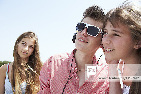Three teenage friends with headphones outdoors