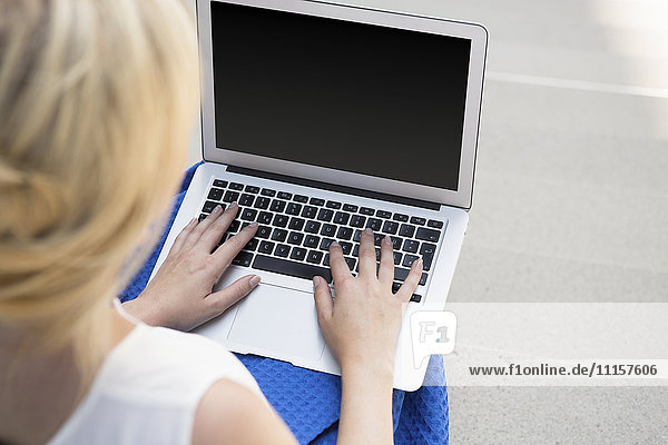 Rückansicht der blonden Geschäftsfrau auf der Treppe mit Laptop Teilansicht