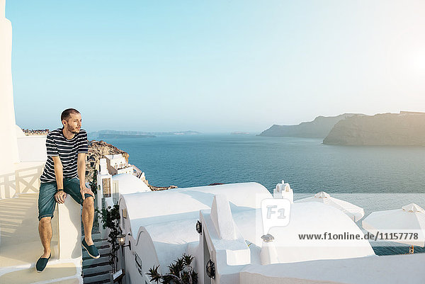 Griechenland  Santorini  Oia  Mann auf einer Wand sitzend  Sonnenuntergang genießend