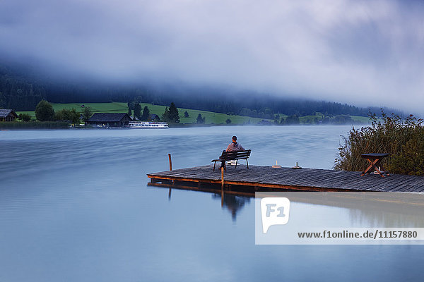 Austria  Carinthia  Man sitting on jetty at Lake Weissensee