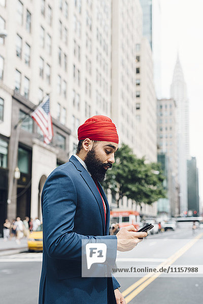 Indischer Geschäftsmann beim Überqueren der Straße in Manhattan  Blick auf Smartphone