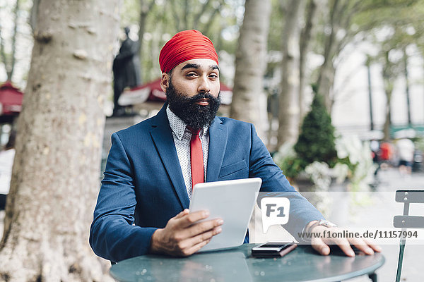 Indischer Geschäftsmann sitzend in Manhattan  mit digitalem Tablett