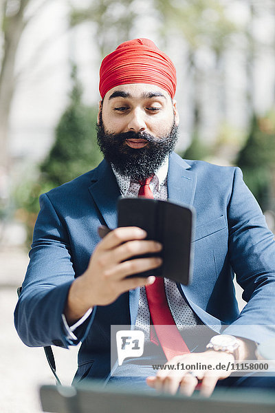 Indischer Geschäftsmann sitzend in Manhattan  mit Smartphone