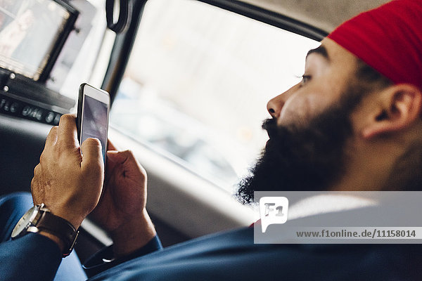 Indischer Geschäftsmann mit Smartphone im Taxi