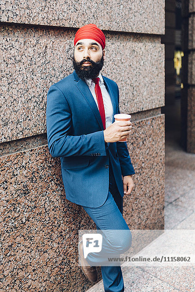 Indian businessman in Manhattan leaning against wall  drinking coffee