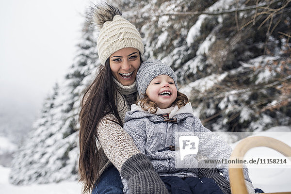 Happy mother with daughter on sledge in winter landscape
