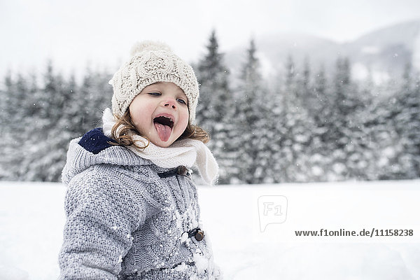 Girl in winter landscape catching snowflakes with her tongue