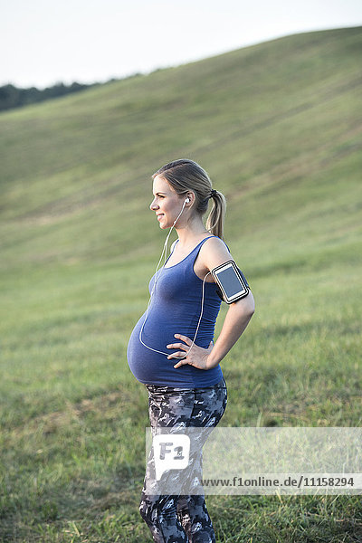 Pregnant woman standing in field taking a break from jogging
