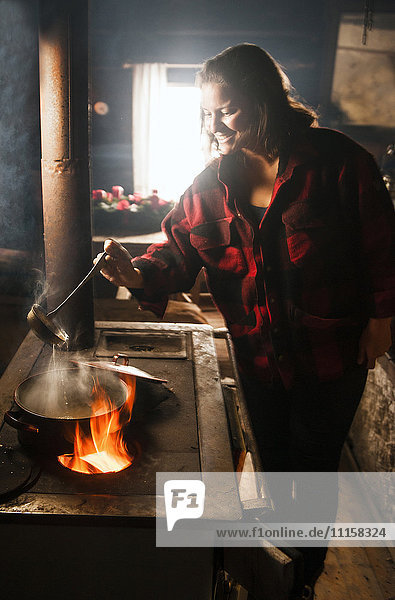 Frau beim Kochen im Ofen in einer Holzhütte