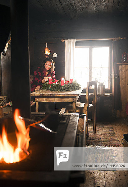 Frau in einer Holzhütte beleuchtet Kerze auf Adventskranz