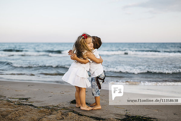 Kleines Mädchen umarmt kleinen Jungen am Strand