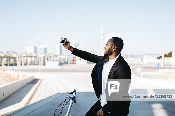 Lächelnder Geschäftsmann mit Fahrrad  der einen Selfie nimmt.
