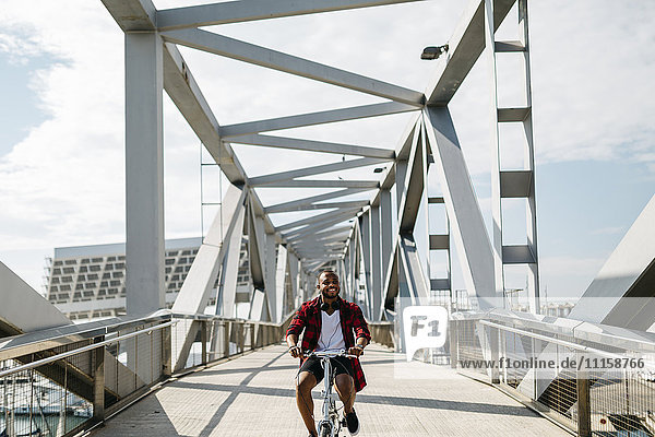 Lächelnder Mann beim Fahrradfahren auf einer Brücke