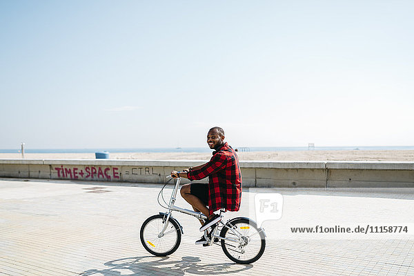 Smiling man riding bicycle near beach