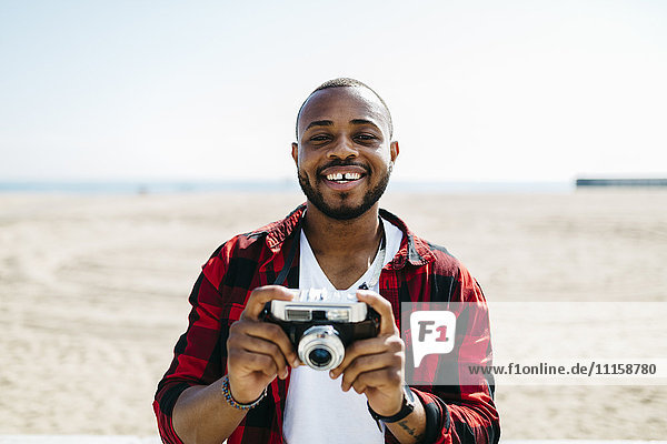Smiling man holding an old-fashioned camera near the beach