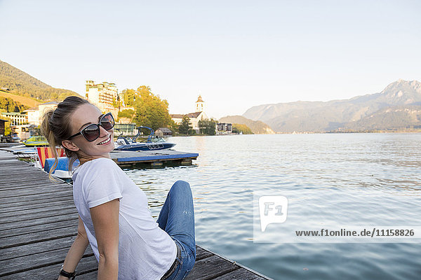 Austria  Sankt Wolfgang  smiling woman sitting on jetty at lake