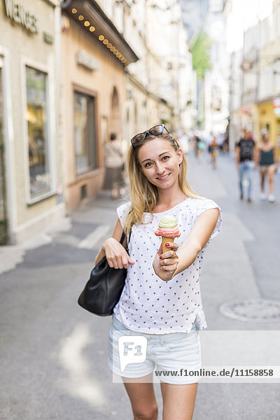 Austria  Salzburg  woman on shopping street offering her ice cream cone to viewer