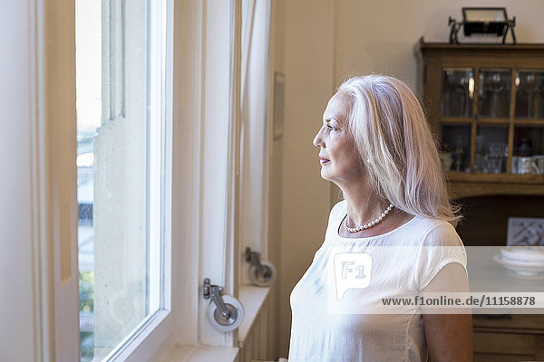 Mature woman looking through window at home