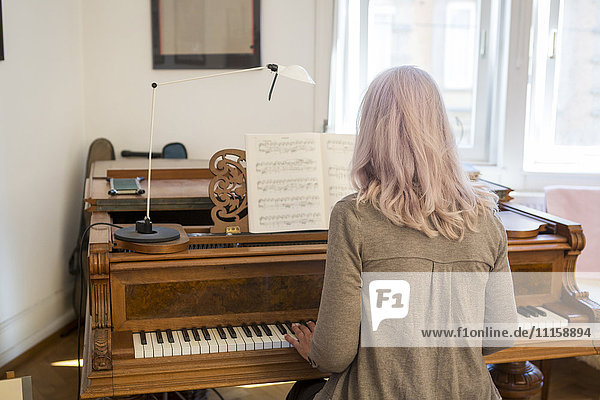 Back view of woman playing piano at home