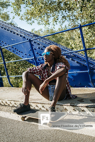 Junge Frau mit Skateboard auf einer Brücke sitzend