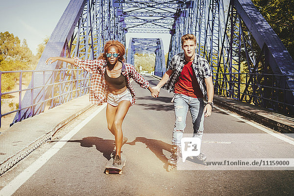 Junges Paar mit Inline-Skates und Skateboardfahren auf einer Brücke