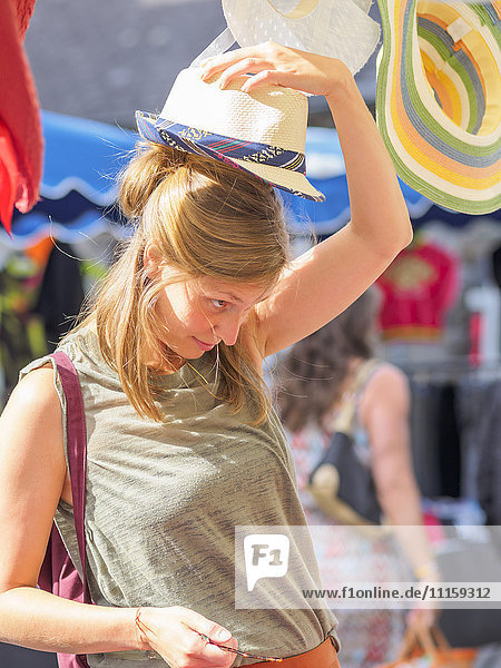 Young woman putting on hat on street market