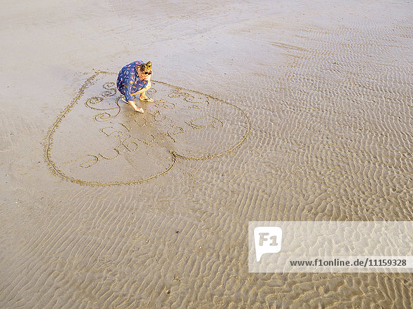Frau am Strand zieht Herz in den nassen Sand