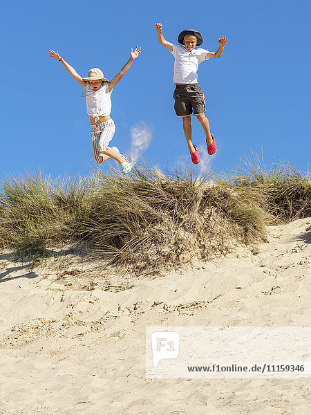 Junge und Mädchen springen von der Stranddüne.