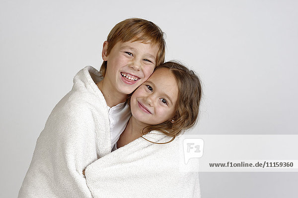 Porträt eines lachenden Jungen  der mit seiner kleinen Schwester eine Decke teilt.