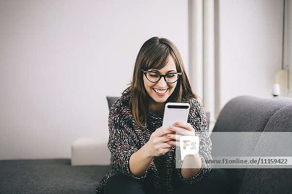 Happy young woman relaxing on the couch looking at her smartphone