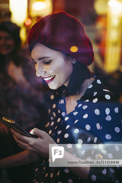 Lächelnde junge Frau mit rotem Hut hinter der Fensterscheibe einer Kneipe am Abend