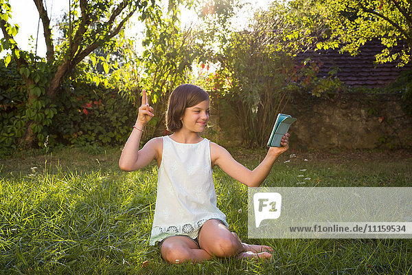 Mädchen sitzt auf einer Wiese und nimmt Selfie mit Tablette