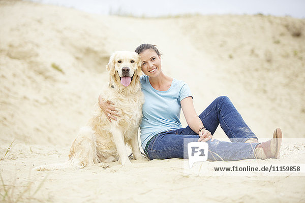 Lächelnde junge Frau mit Hund im Sand