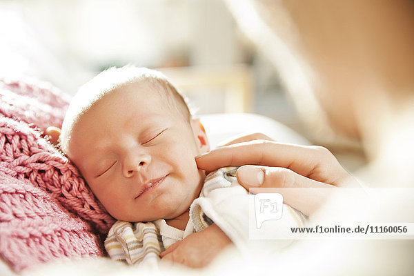 Schlafende Neugeborene  die von einer Hand berührt werden.
