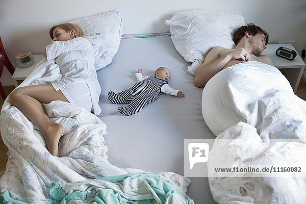 Eltern schlafen mit Neugeborenen im Bett