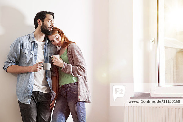 Smiling young couple holding cups in an apartment