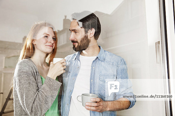 Lächelndes junges Paar bei einer Kaffeepause hinter der Fensterscheibe