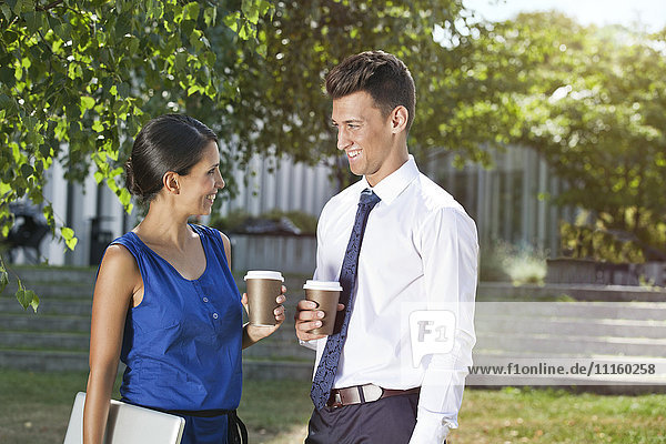 Lächelnde Geschäftsfrau und Geschäftsmann mit Kaffee zum Mitnehmen im Freien